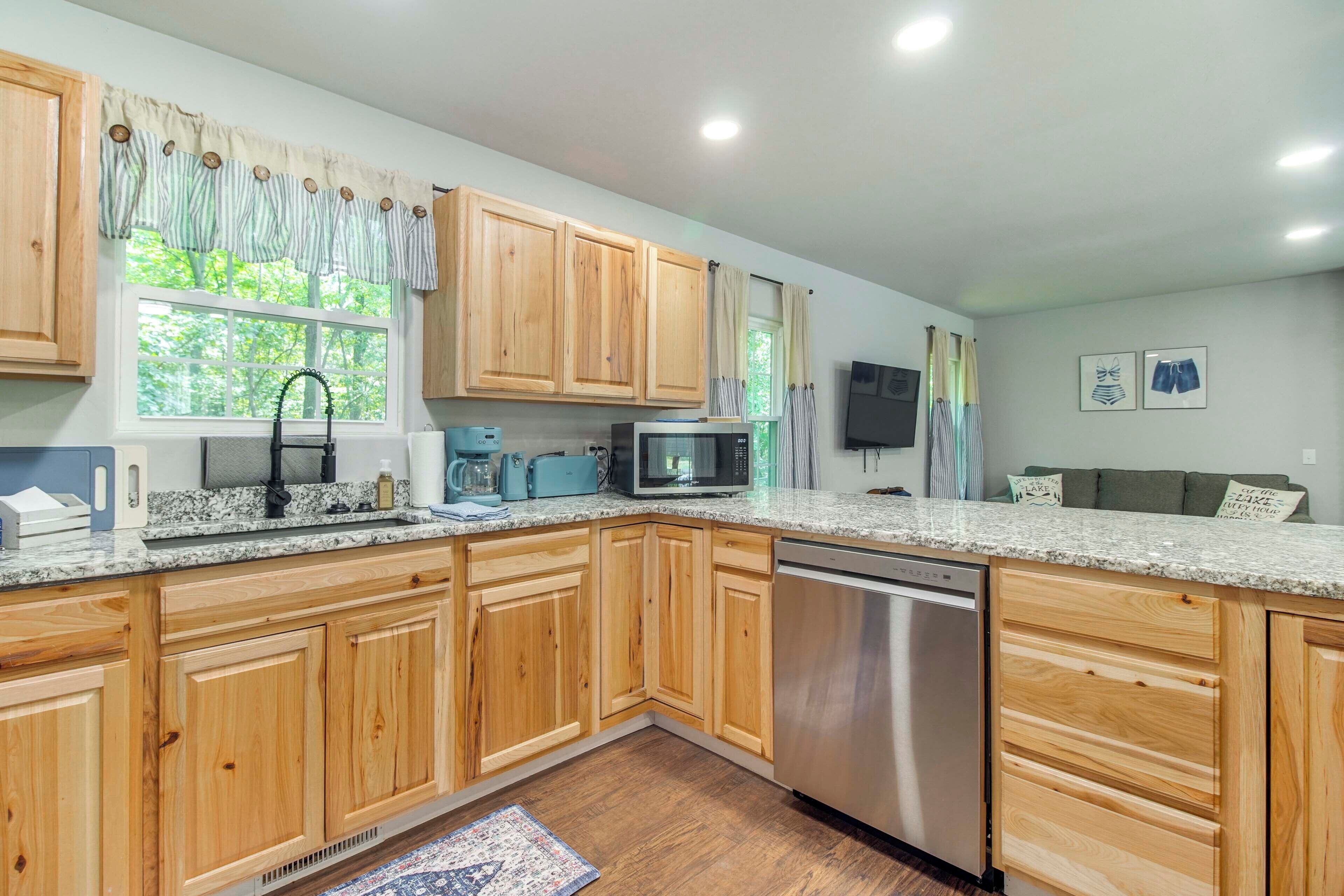 A modern kitchen with wooden cabinets, a granite countertop, a dishwasher, and a window with curtains.