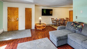 A living room with a gray sofa, wooden flooring, a glass coffee table, and a TV mounted on the wall.