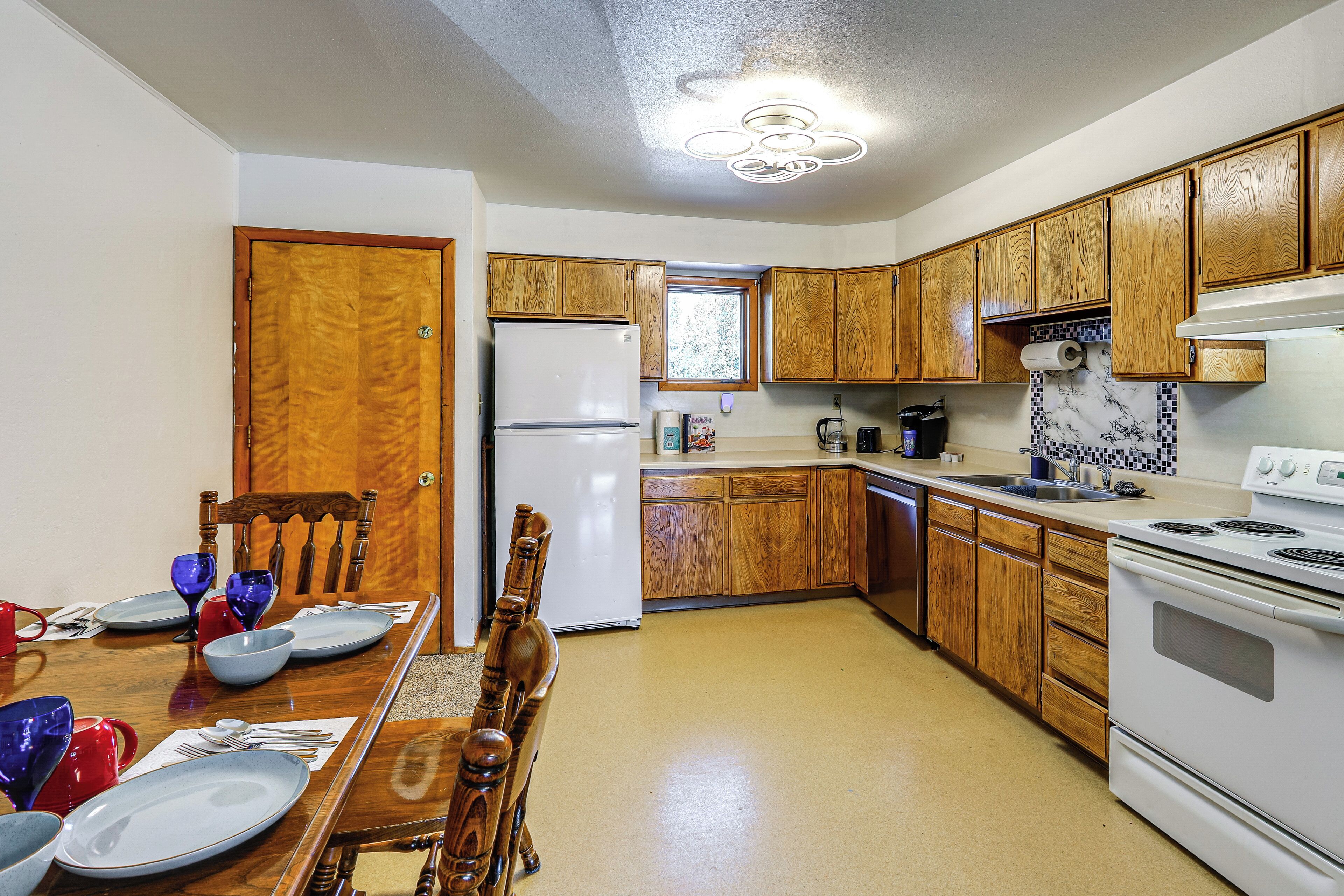 A kitchen with wooden cabinets, a refrigerator, a stove, and a dining table set with plates and bowls.