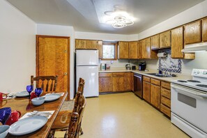 A kitchen with wooden cabinets, a refrigerator, a stove, and a dining table set with plates and bowls.