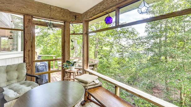 Une terrasse en bois avec une table et des chaises, un banc et de grandes fenêtres donnant sur les arbres environnants.