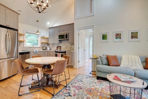 A modern kitchen with a dining area, a living room with a sofa, and a hallway with framed pictures.