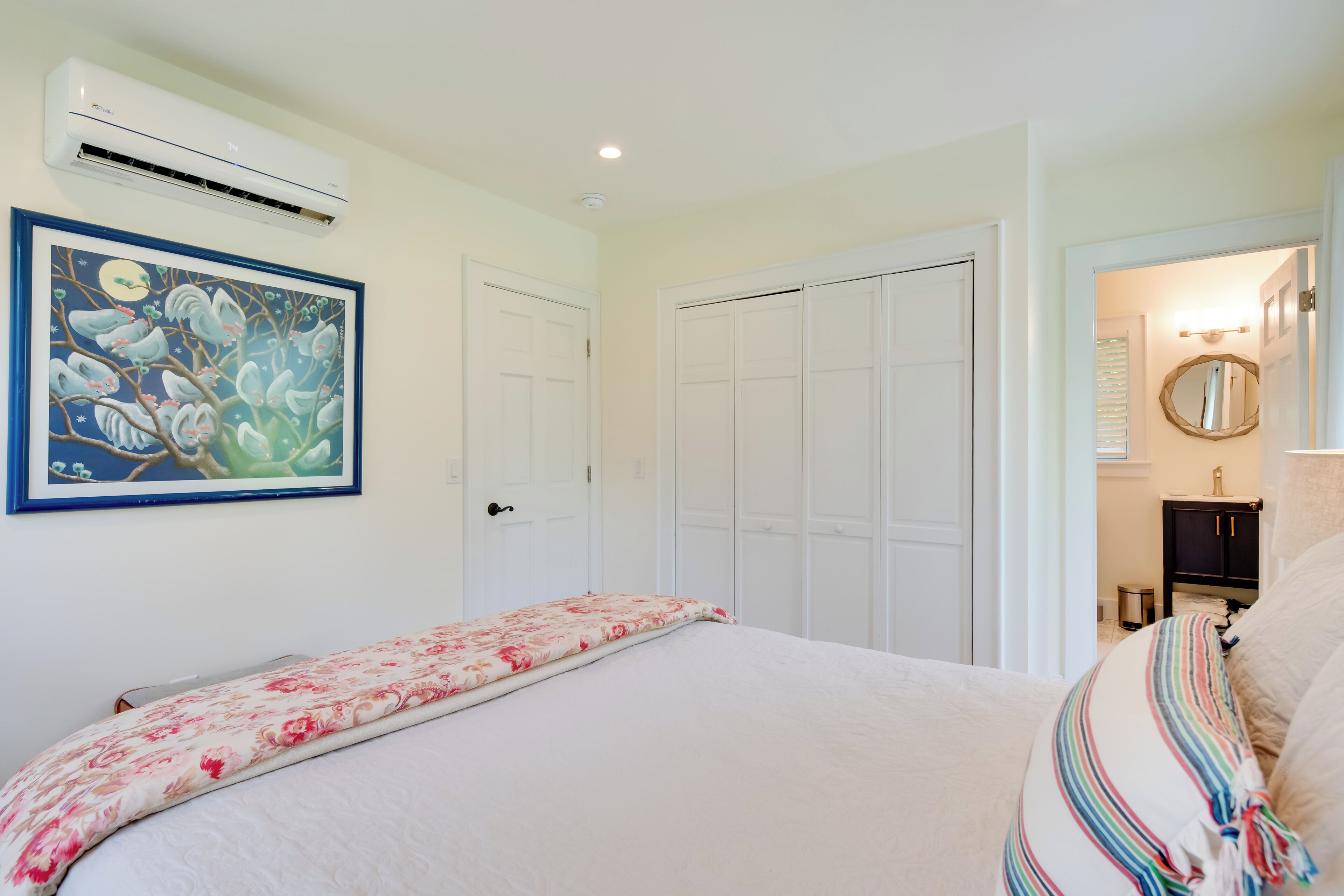 A bedroom with a bed, a wall-mounted air conditioner, a door, and a framed picture.
