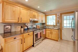 A kitchen with wooden cabinets, a gas stove, an oven, a stainless steel refrigerator, and a window providing natural light.