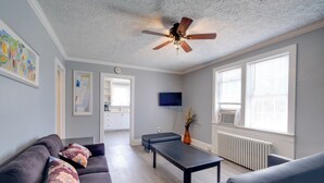 Ein modernes Wohnzimmer mit Deckenventilator, Flachbildfernseher und Essbereich mit Tisch und Stühlen.