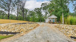 A gravel driveway leading to a small cabin with a porch, surrounded by trees and a wooden fence.