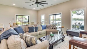 A spacious living room with a sectional sofa, a coffee table, and a view of a lake through large windows. - Lake Wapogasset Home w/ Dock: 7 Mi to Amery (Amery)