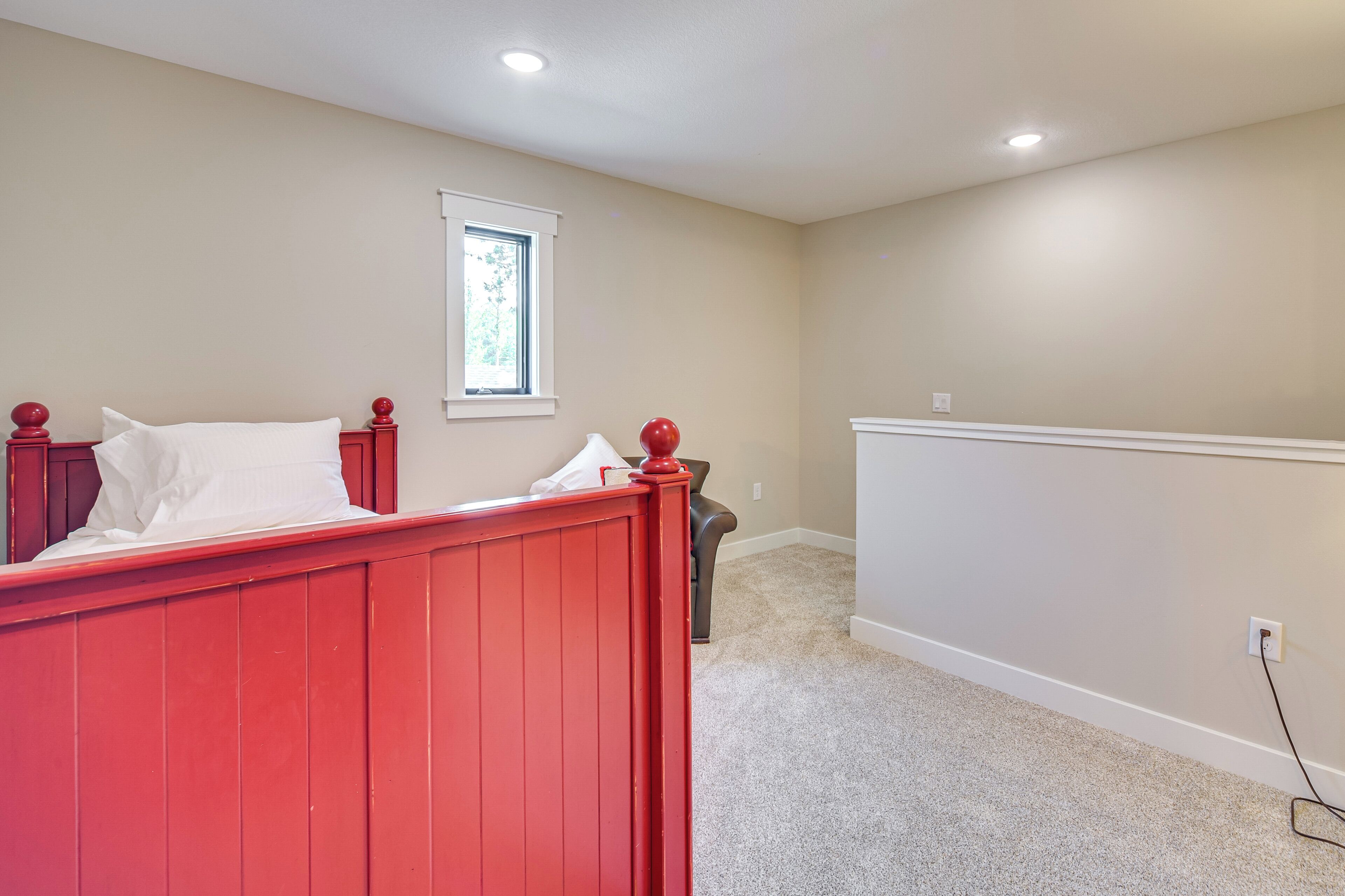A bedroom with a red bed, a window, and a carpeted floor.