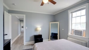 A bedroom with a bed, a dresser, a mirror, a nightstand, a lamp, and a window with an air conditioner. - Near Loudoun Wine Trail: Apt w/ Restaurant On-site (Hamilton)