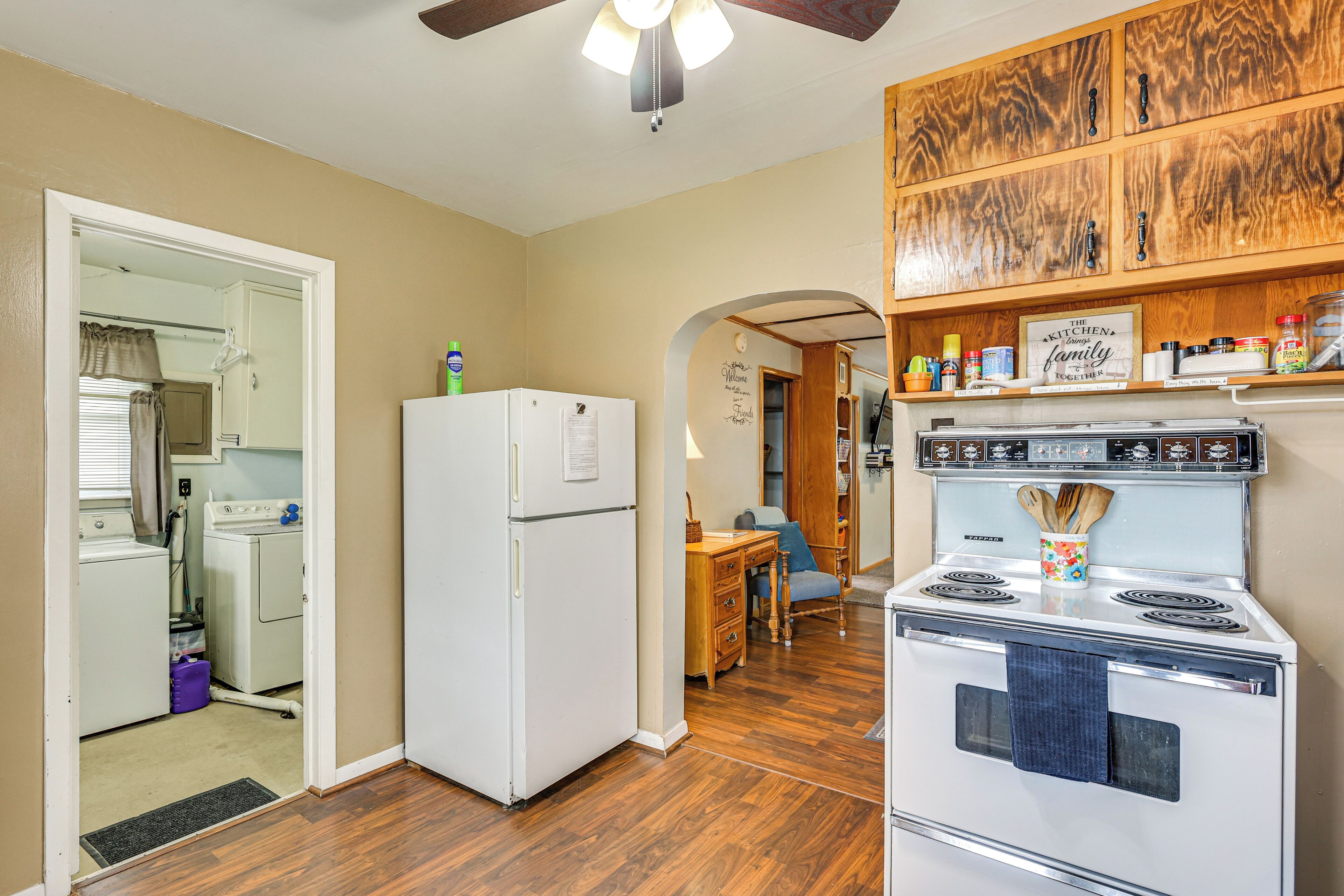A kitchen with wooden cabinets, a white refrigerator, a stove, and a dining area with a table and chairs.