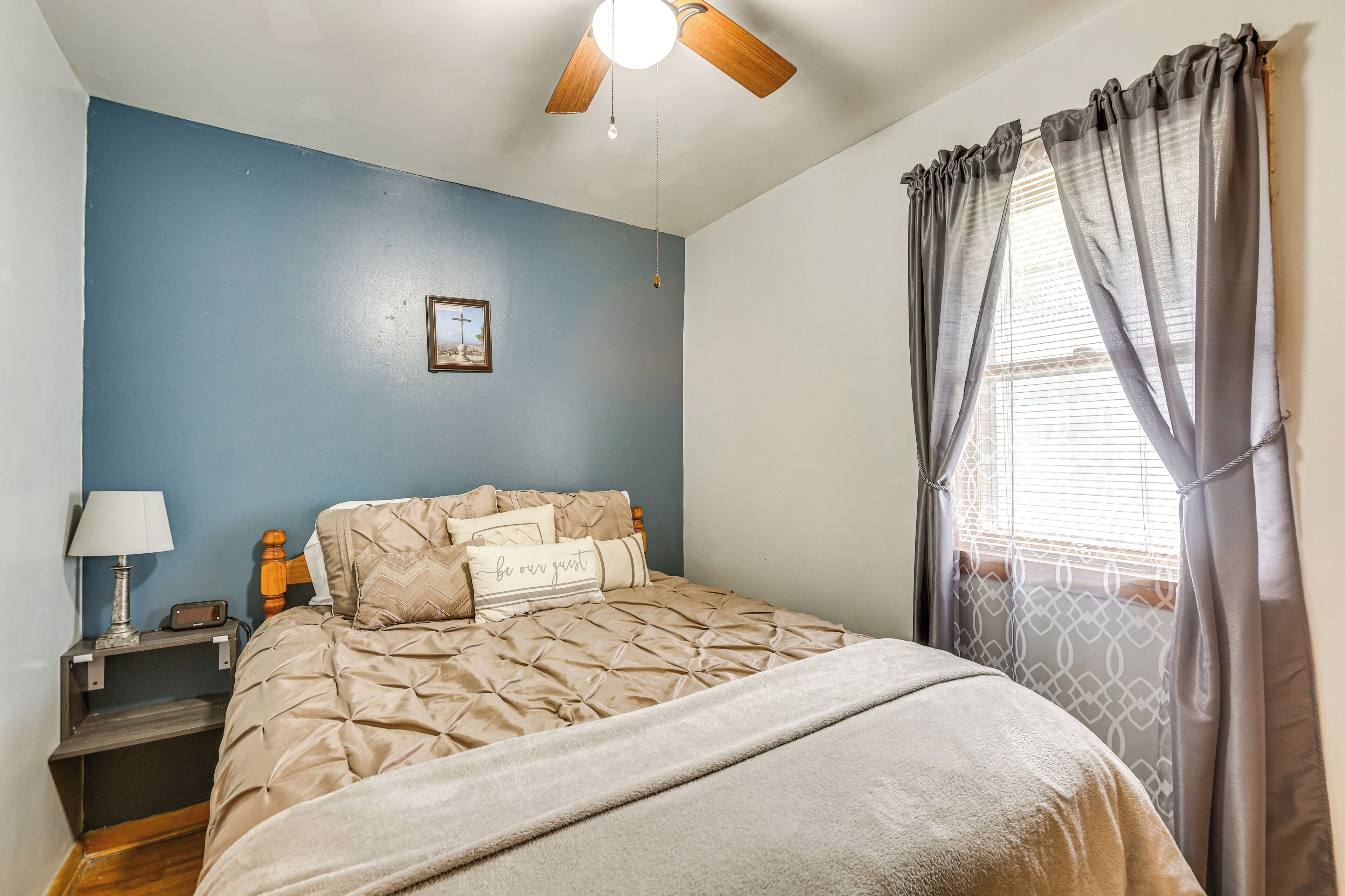 A bedroom with a bed, a nightstand, a lamp, a ceiling fan, and a window with curtains.