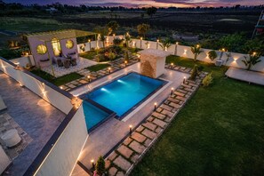 A rectangular swimming pool with a stone border, surrounded by a well-maintained lawn and garden. - Sanjeevani Farms, Bhopal : A Luxury 5 Bedroom Private Pool Villa (Sehore)