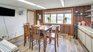 En matplats med trämöbler, ett stort fönster med växter och ett köksområde med skåp och vitvaror.