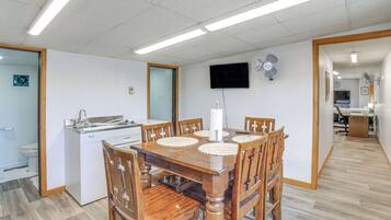 A dining area with a wooden table and chairs, a white sink, and a television mounted on the wall.