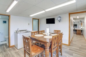 Un coin repas avec une table et des chaises en bois, un évier blanc et un téléviseur fixé au mur.