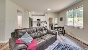 A spacious living room with a leather sofa, a dining table with chairs, and a large window providing a view of the outdoors. - Explore Alaskas Playground: Modern Wasilla Escape (Wasilla)