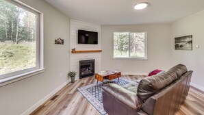 A living room with a fireplace, a television mounted on the wall, and a large window offering a view of the outdoors. - Explore Alaskas Playground: Modern Wasilla Escape (Wasilla)