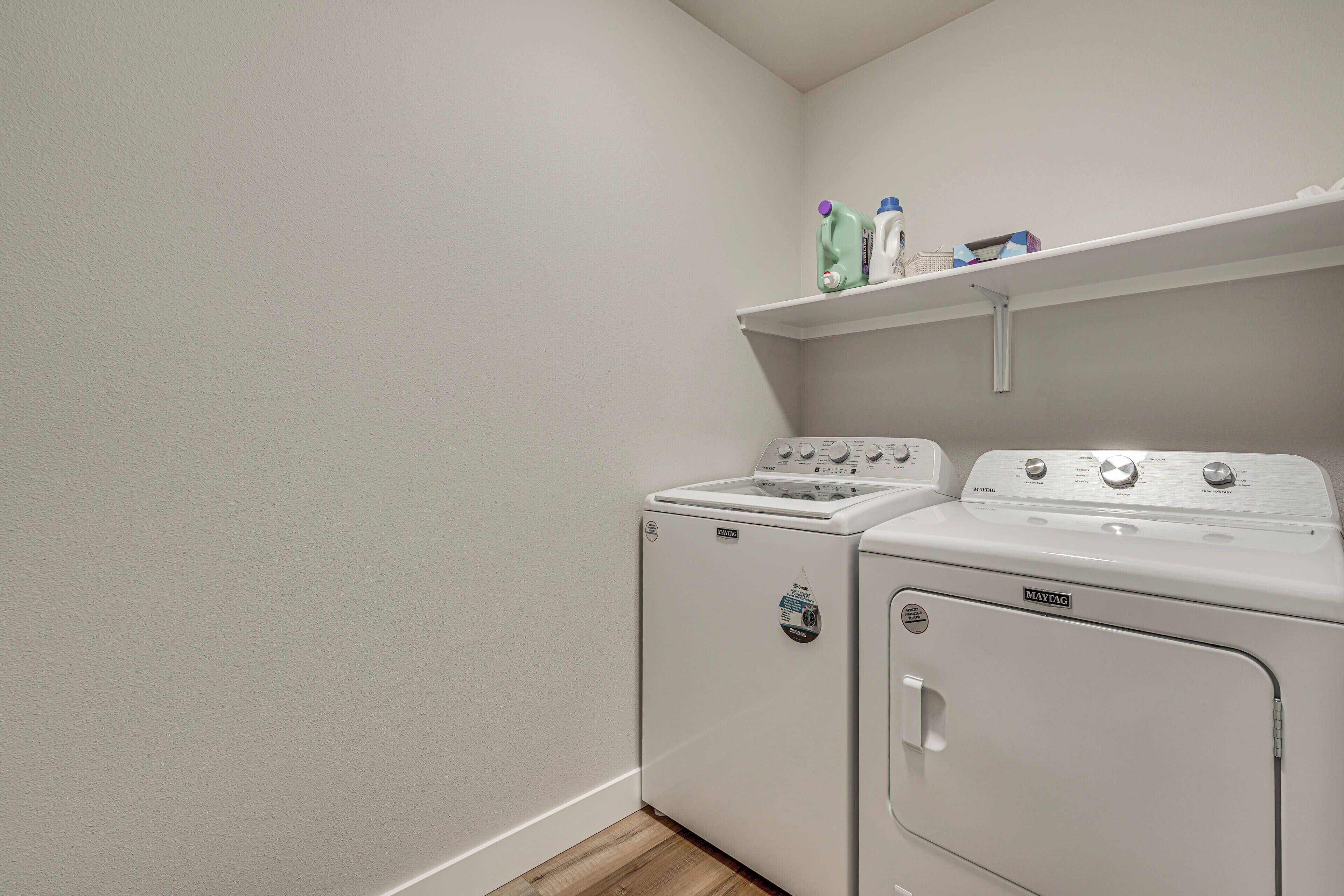 A laundry room with two Maytag washers and dryers, a shelf with cleaning supplies, and a white wall.