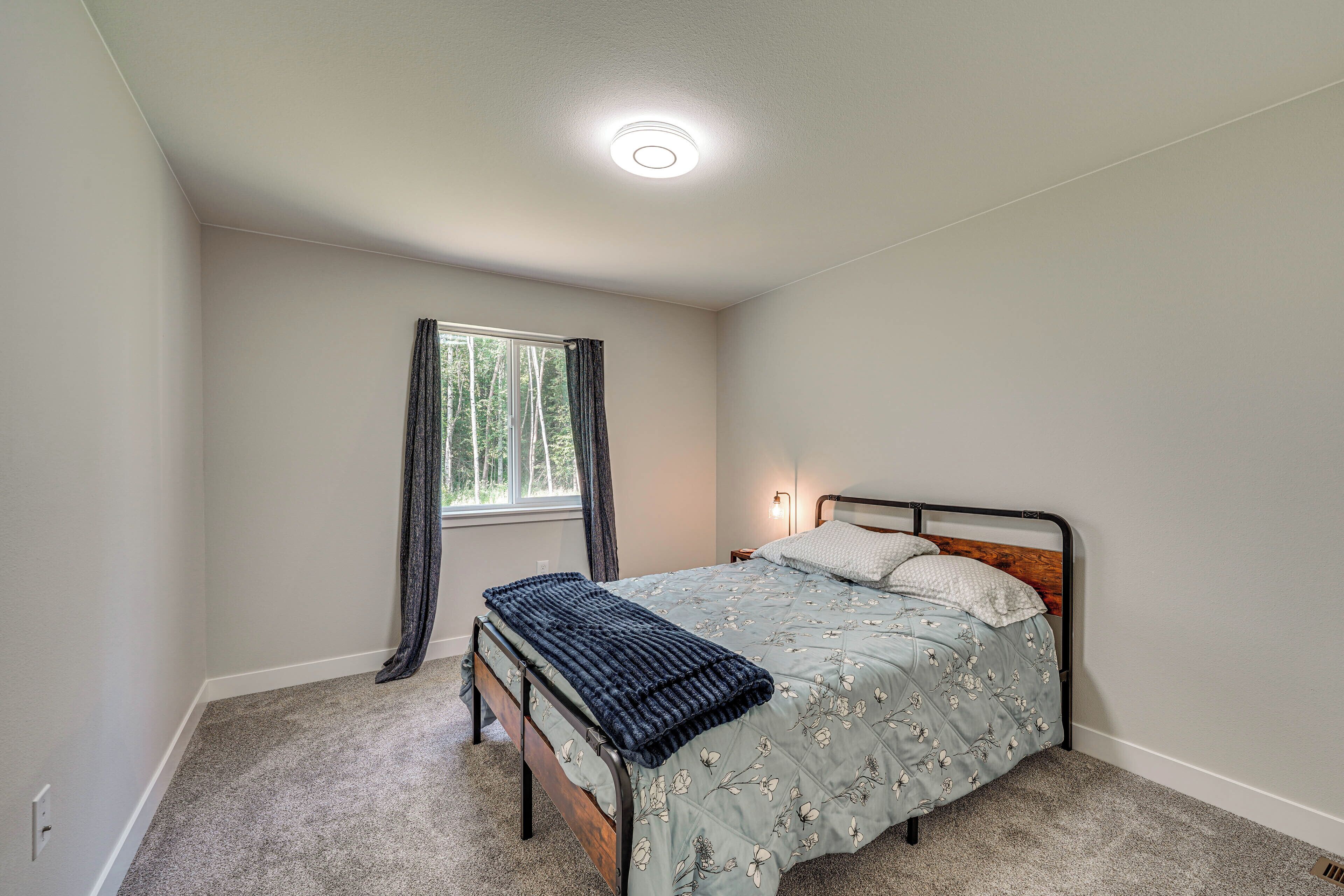 A bedroom with a bed, a window with curtains, a bedside lamp, and a ceiling light.