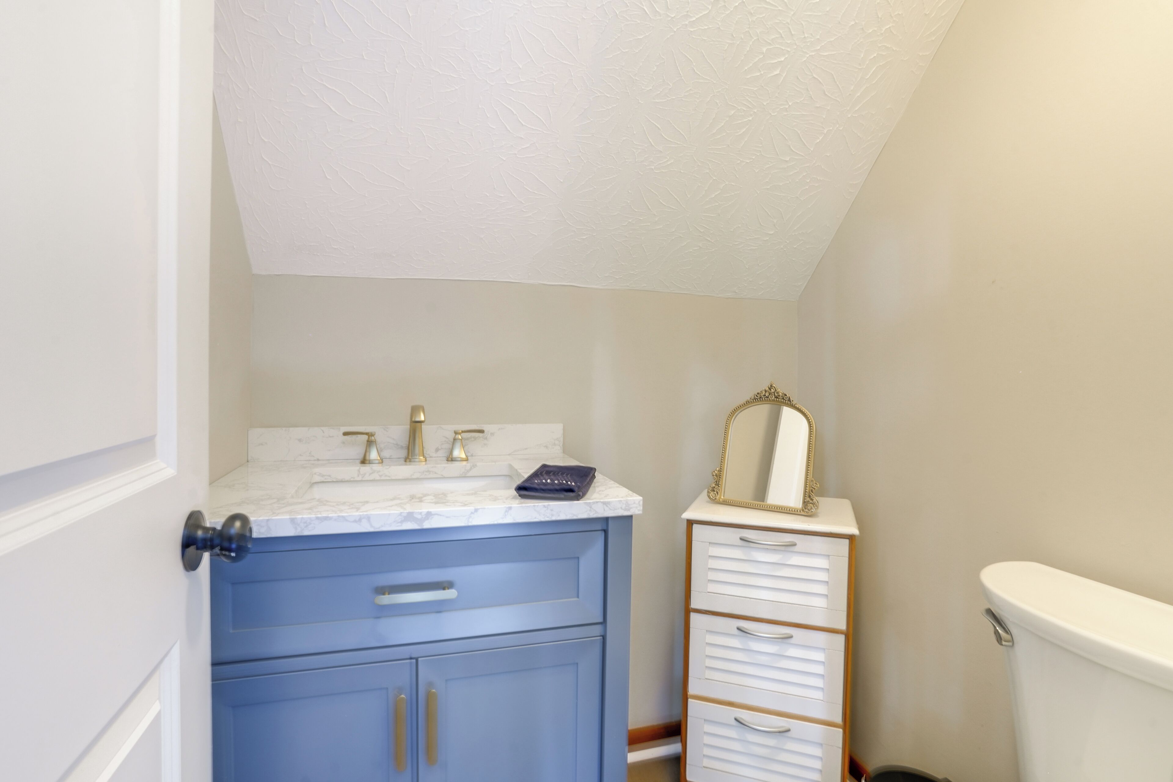 Et badeværelse med en marmorvask, et blått toiletbord, et hvidt toilet og et spejl med gylden ramme.