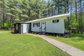 A single-story mobile home with a porch, a small attached garage, and a picnic table in a wooded area. - Hiking & ATV Trails On-site: Adirondacks Abode (Brantingham)