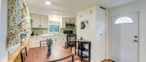 Una cocina compacta con muebles blancos, un microondas y una mesa de comedor de madera.