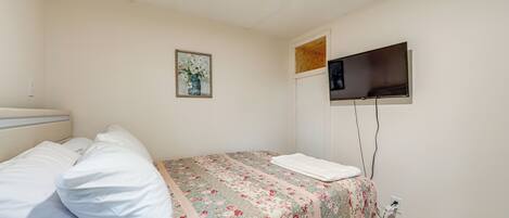 A bedroom with a bed, a flat-screen TV mounted on the wall, and a power outlet on the wall.