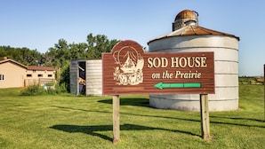 Une enseigne indiquant « SOD HOUSE on the Prairie », avec une grange rustique et un silo en arrière-plan.