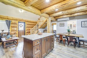 A rustic cabin interior with a wooden staircase, a kitchen island, and a dining area.