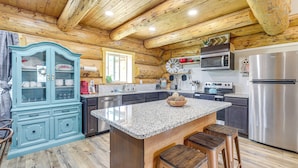 Una cocina con vigas de madera, encimeras de granito, una isla central con taburetes y electrodomésticos modernos.