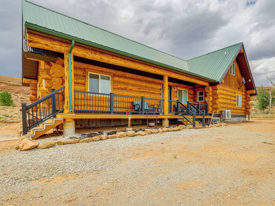 A log cabin with a porch, a staircase, and a green roof.
