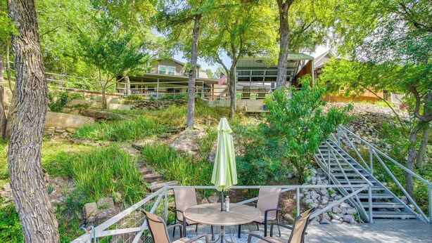 A deck with a round table and chairs, surrounded by a railing, overlooking a landscaped area with trees and a building in the background. - Waterfront Lake Bridgeport Home w/ Private Dock (Bridgeport)