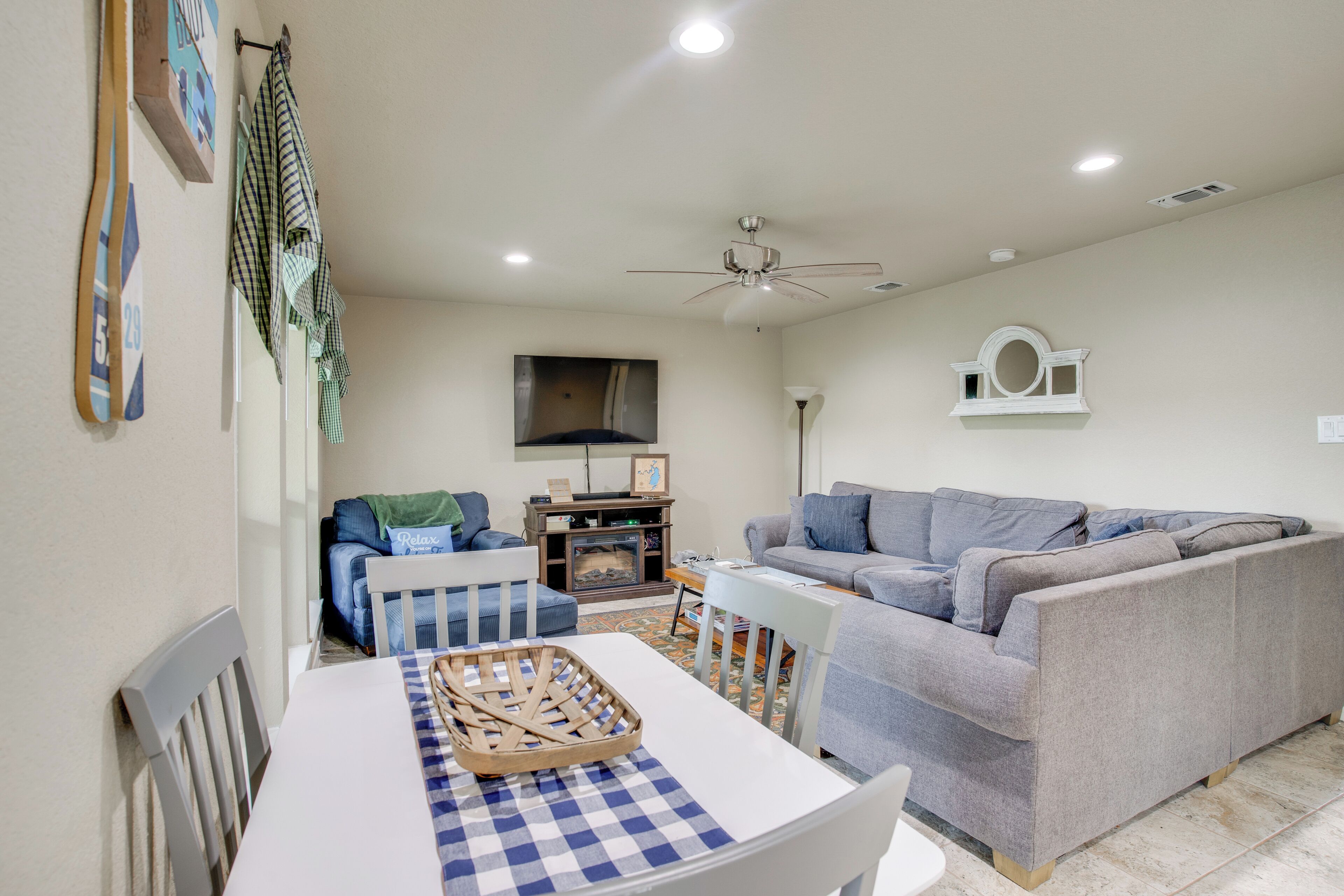A living room with a grey sofa, a white table with a checkered tablecloth, and a ceiling fan.