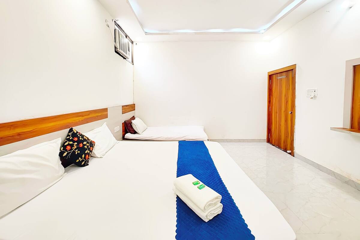 Quarto de hotel com duas camas, um tapete azul, uma porta de madeira e uma luminária no teto.