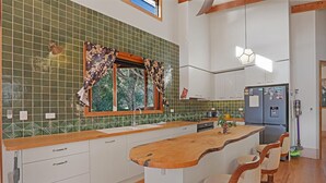 Eine Küche mit grüner Fliesenrückwand, Holz Arbeitsplatte, weißen Schränken und einer eingebauten Kochinsel mit Barhocker.