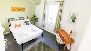 Een slaapkamer met een bed, nachtkastje, spiegel en een raam met gordijnen.