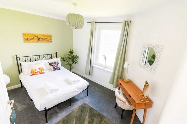 Une chambre à coucher avec un lit, une table de chevet, un miroir et une fenêtre avec des rideaux.
