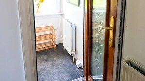 Een hotelingang met een vluchtwegbord, een houten deur, een radiator en uitzicht op buiten.