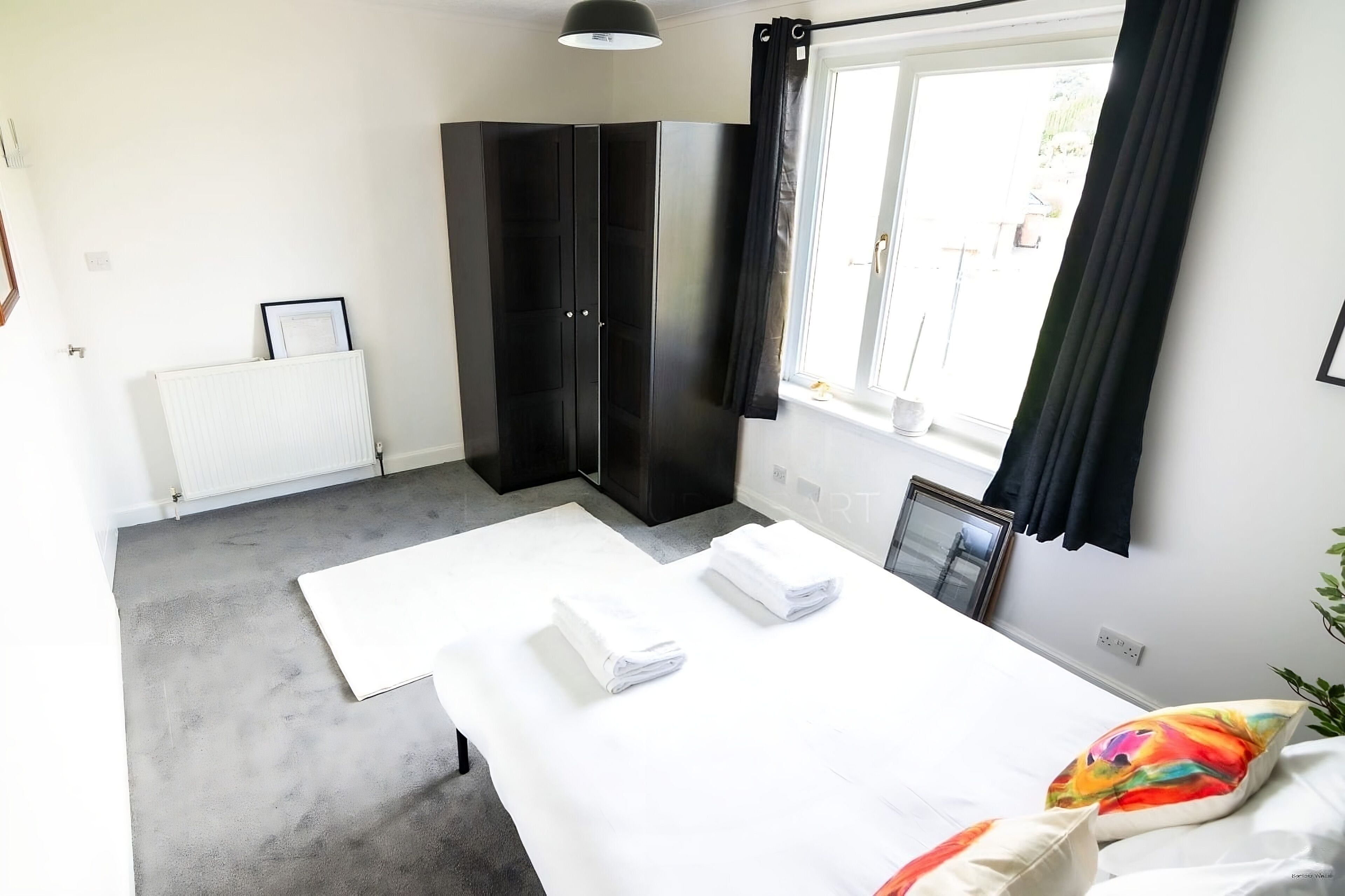 Quarto com cama, radiador, guarda-roupa e janela com cortinas.