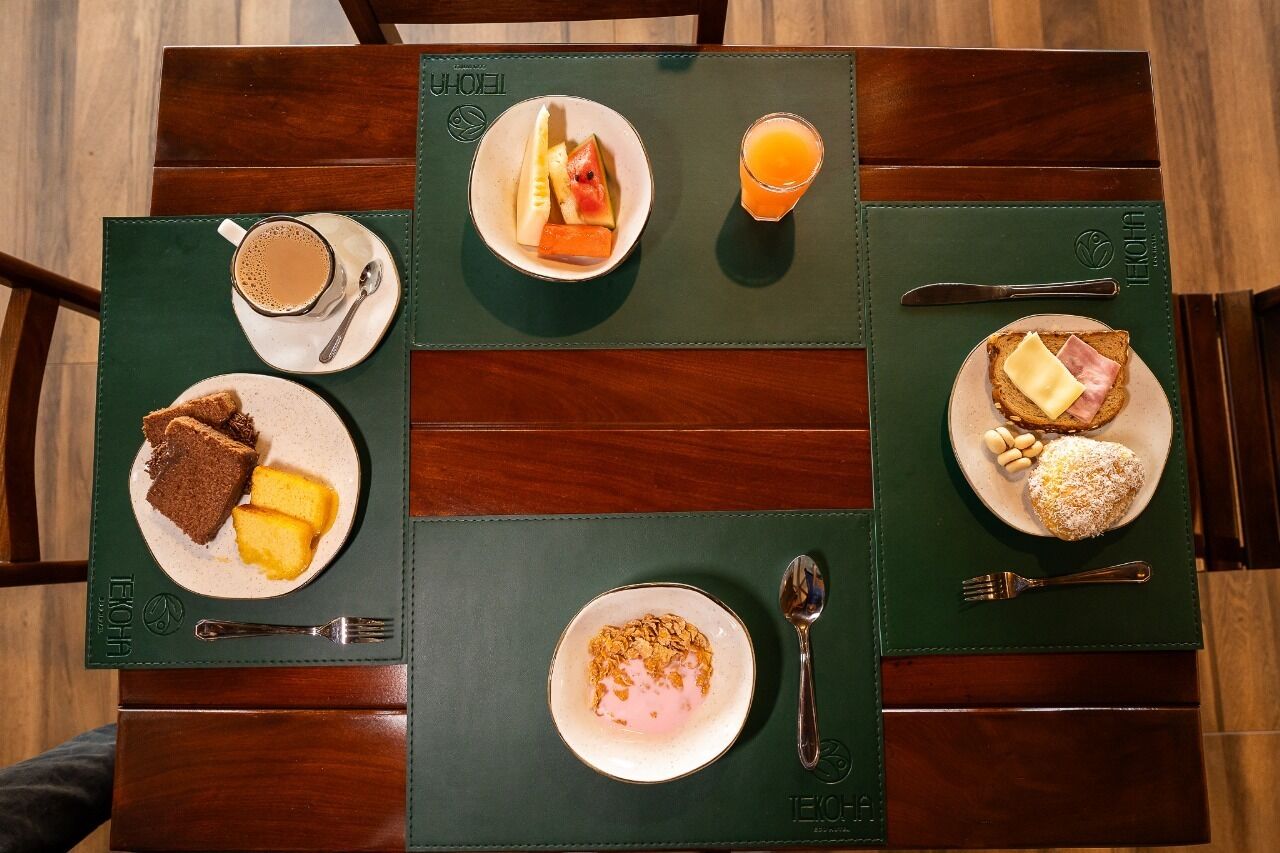 A breakfast setting with a coffee, fruit, toast, and cereal on a wooden table with green placemats.