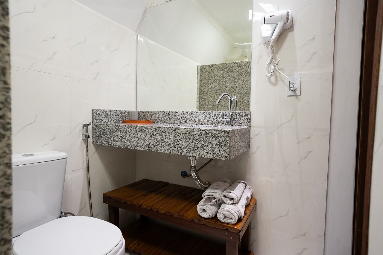 A bathroom with a white toilet, a granite sink, a wooden bench, and a hairdryer mounted on the wall.