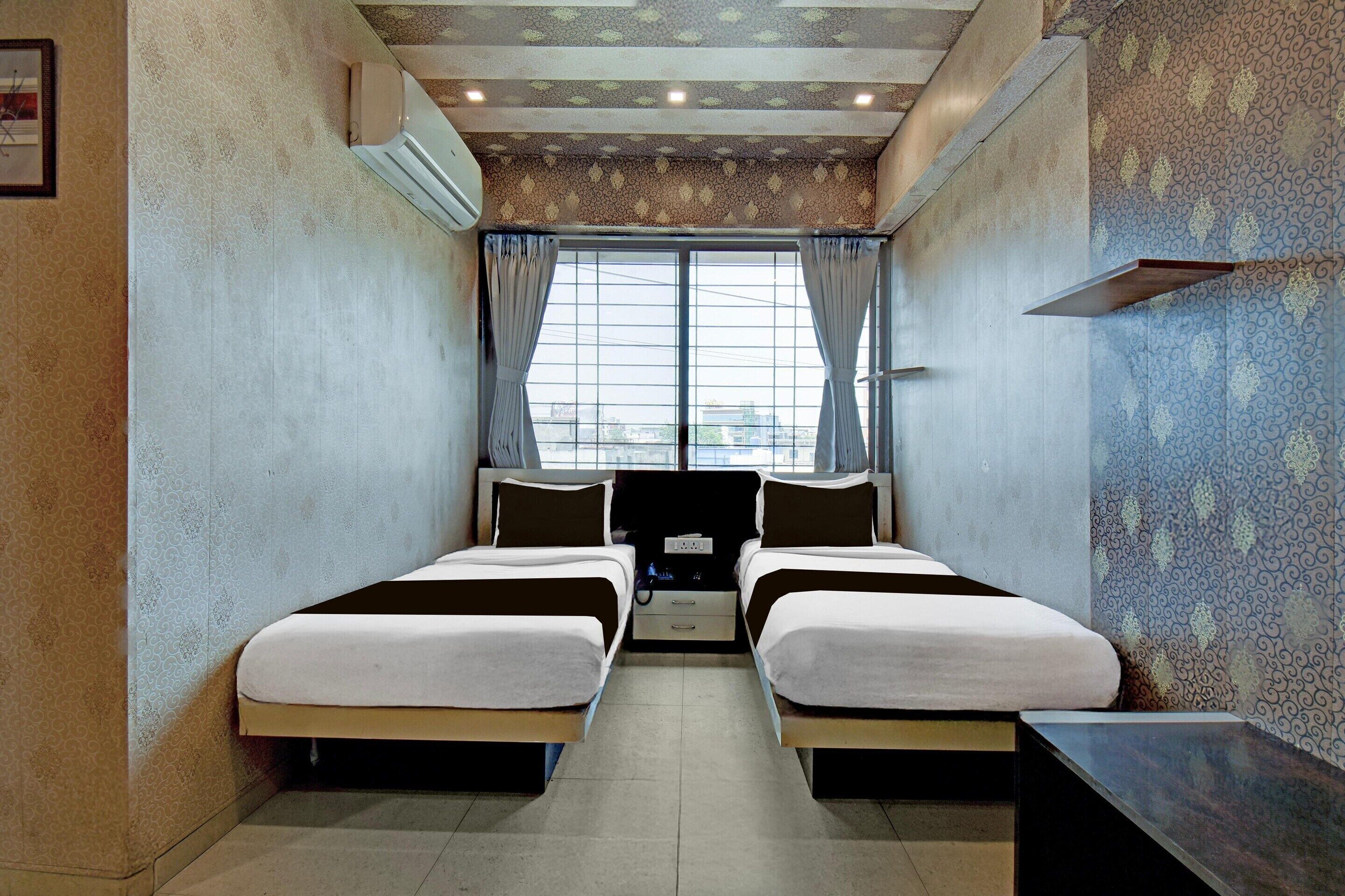 A hotel room with two beds, a TV, a desk, and a window with curtains.