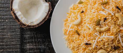 A plate of yellow rice with raisins and cashew nuts on a wooden surface.