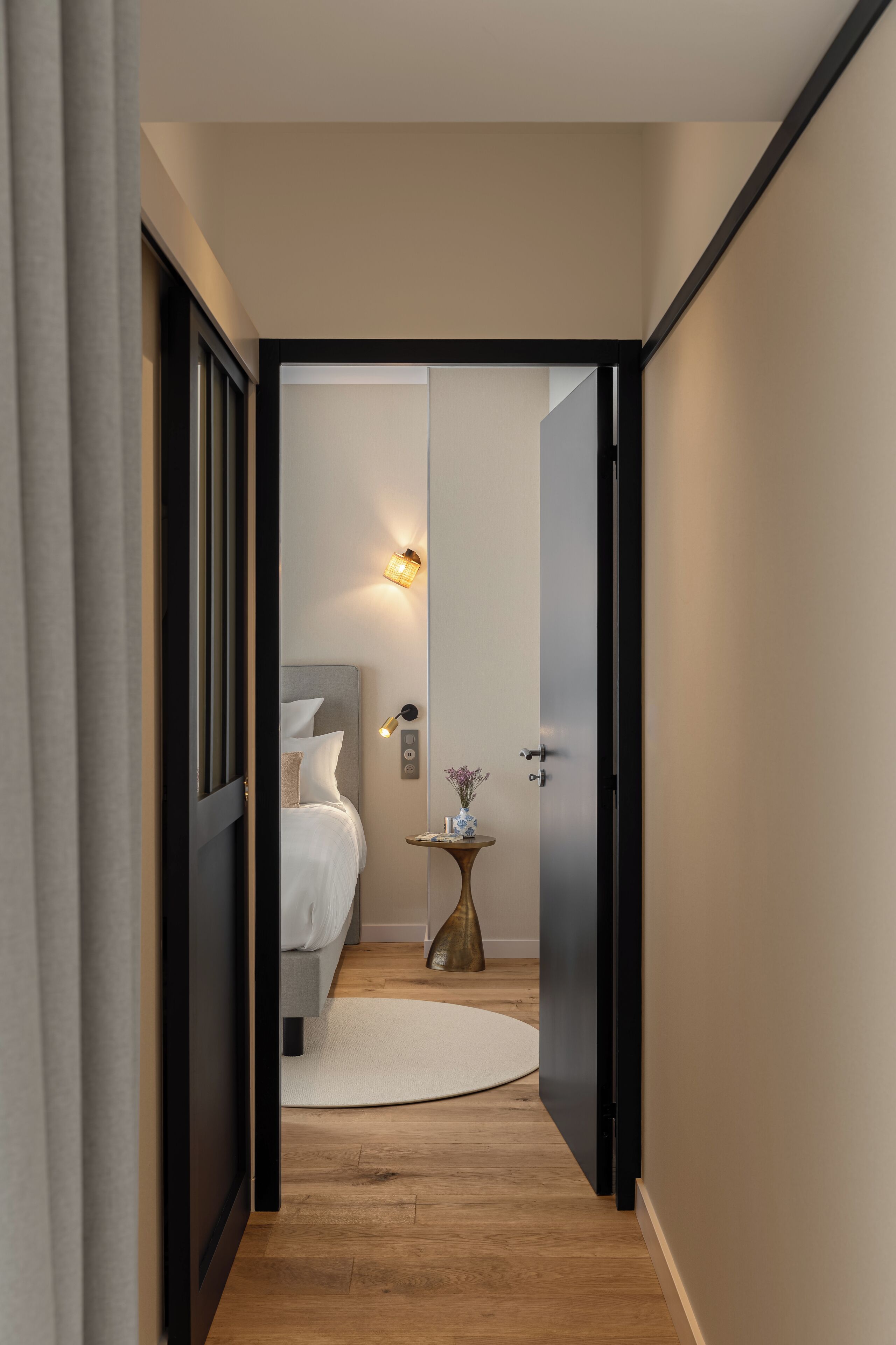 Un pasillo estrecho que conduce a un dormitorio con cama, mesita de noche e iluminación en la pared.