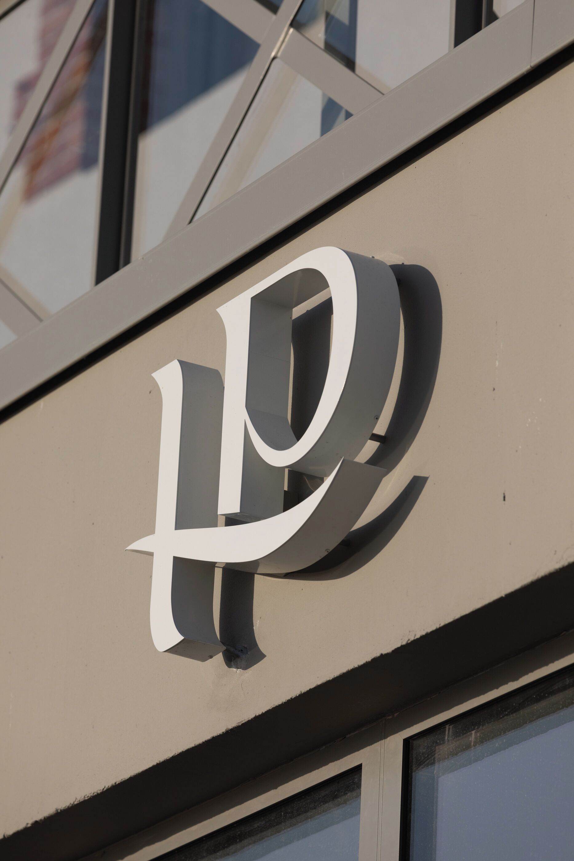 Ein Gebäudeschild mit einem großen, stilisierten Buchstaben 'P' an einer beigen Wand.