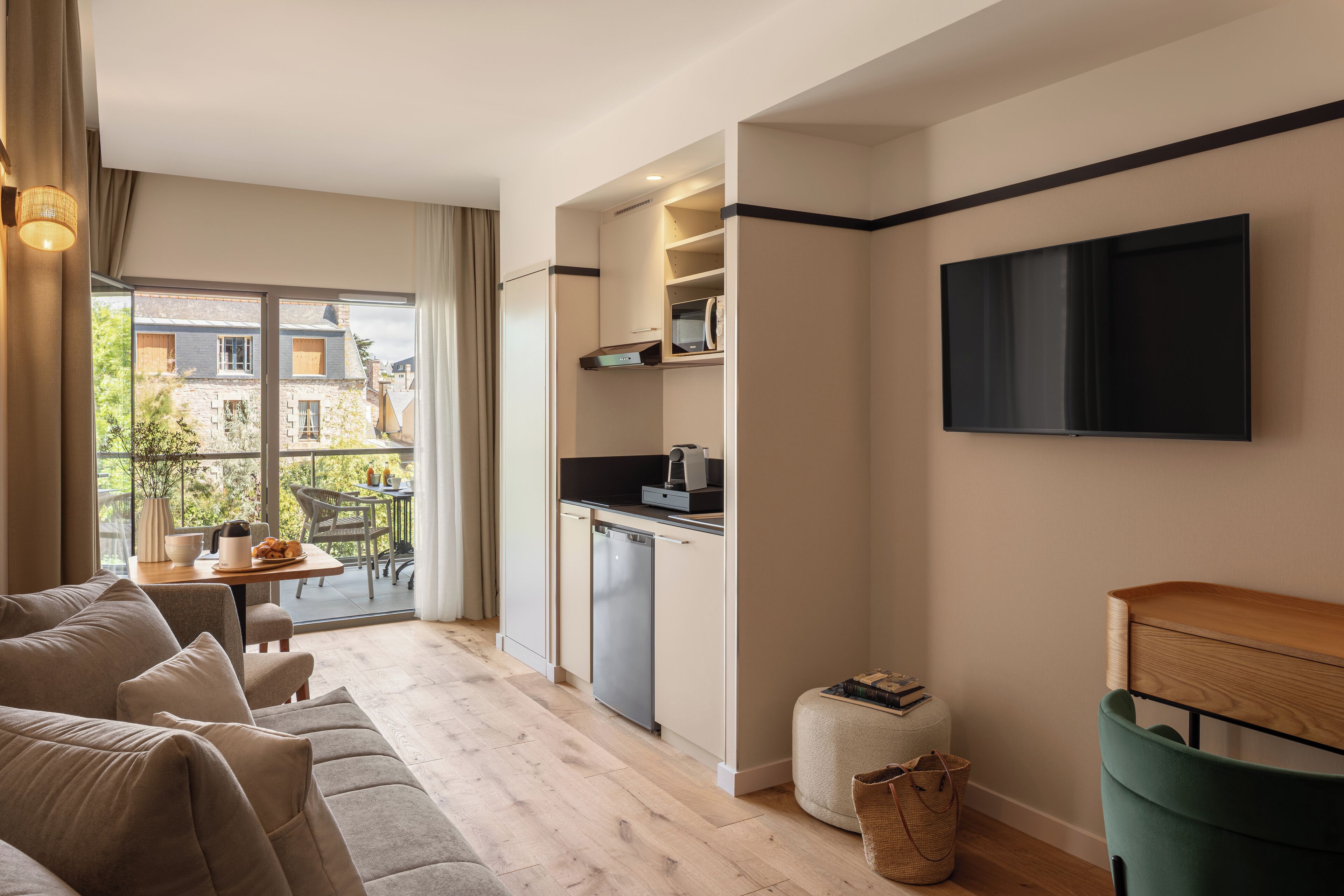 Een modern appartement met een woonkamer, kitchenette en een balkon met uitzicht op gebouwen.