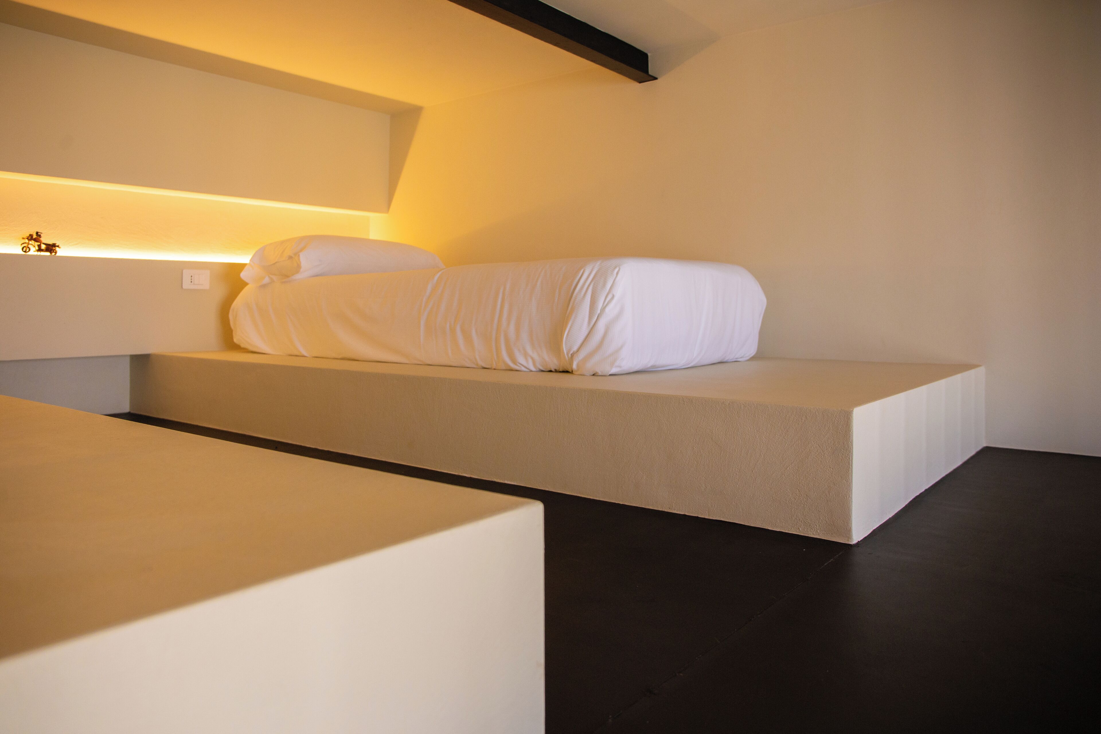 Un dormitorio minimalista con una cama baja de plataforma, una mesita de noche y una lámpara fijada a la pared.