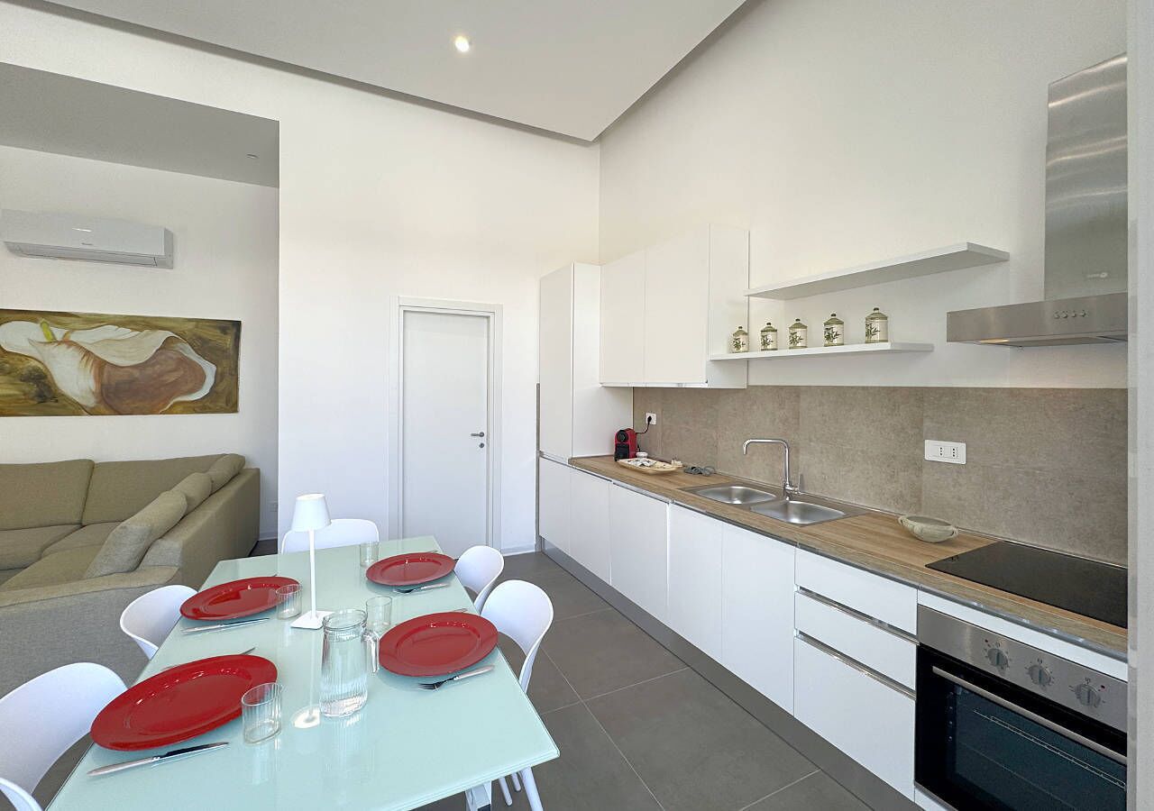 A modern kitchen with white cabinets, a stainless steel oven, and a dining area with a table set for four.
