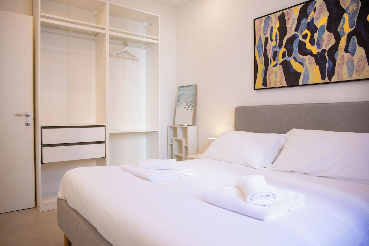 Une chambre d’hôtel avec un lit bien fait, un dressing et un tableau accroché au mur.