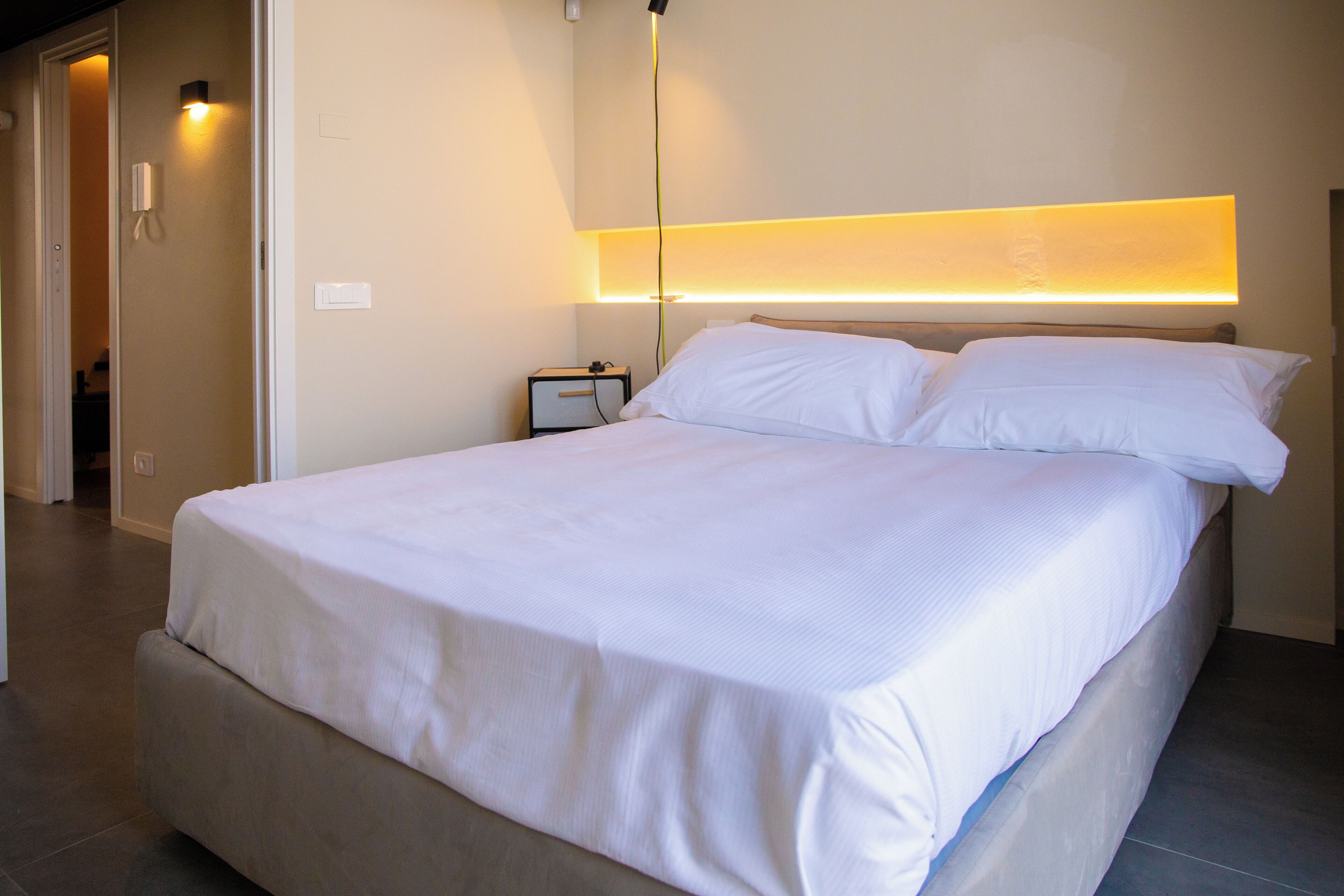 A modern hotel room with a large bed, a bedside table, and a wall-mounted light fixture.